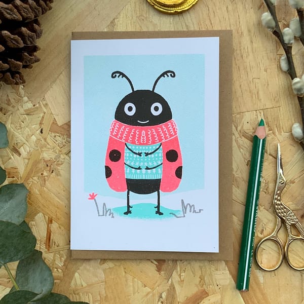 Photograph of a Risograph print greetings card with a ladybird character standing in the snow.